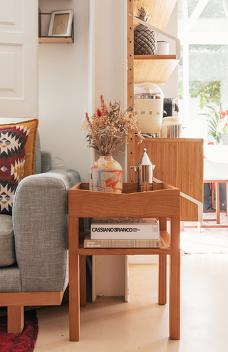 INDRA wooden side table with a woven cane shelf beside a sofa.